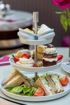 a three tiered tray with sandwiches and desserts on it, sitting on a table