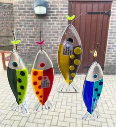 three colorful glass fish hanging from hooks on a brick wall in front of a door