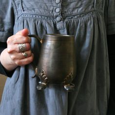 a woman is holding a metal cup in her right hand and wearing a silver ring