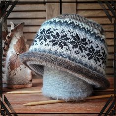 a knitted hat sitting on top of a wooden table next to two knitting needles