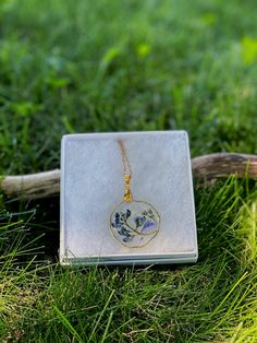 a necklace with a flower on it sitting in the grass next to a piece of wood