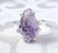 The beautiful rough amethyst crystal in this ring is completely gorgeous! Totally untreated and uncut, the natural facets and smooth crystal faces reflect light, while inside the crystal glitters with ridges and rainbow-like inclusions. The fascinating stone is set in a hand-made sterling silver claw setting and placed on a hammered sterling silver band. This lovely, slightly rustic ring would be a perfect gift for a February baby (or the mother of one!), or for someone special who deserves a tr Purple Crystal Ring, Silver Amethyst Crystal Ring As Gift, Elegant Silver Amethyst Crystal Ring, Unique Amethyst Crystal Ring, Elegant Handmade Purple Crystal Ring, Unique Silver Amethyst Crystal Ring, Raw Stone Engagement Rings, Amethyst Wedding Rings, Birthstone Ring Mothers