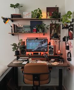 a desk with a computer, speakers and plants on the shelf above it is also a bed