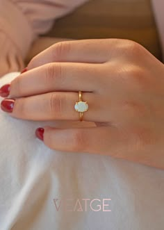 a woman's hand wearing a gold ring with an opal stone in the middle