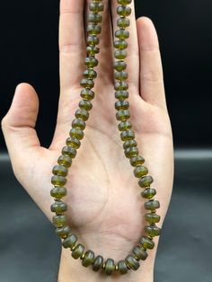 a hand holding a strand of green glass beads