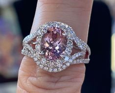 a close up of a person's hand holding a ring with an oval shaped pink diamond