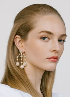 a woman with blonde hair and blue eyes wearing large pearl drop earrings on her ear