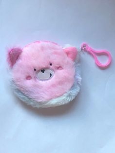 a pink teddy bear keychain on a white surface with a pink clip hanging from it's side