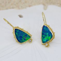 Escape into the beauty of the sea with these stunning Opal & Diamond Earrings. Crafted from 18K granulated gold and adorned with gorgeous blue-green opals and two small diamonds, these earrings shimmering like the rolling waves of a distant shore. Treat yourself to a little oasis with these charming ocean-inspired earrings 18KY granulated earrings with 2 opal doublets weighing 8.42cts and accented with .06cttw of VS/GH diamonds.Dimensions: 7/8” x 9/16” (24mm x 15mm) excluding earwire Yellow Gold Opal Gemstone Earrings, Ocean Inspired Earrings, Boulder Opal Jewelry, Green Opal, Ocean Inspired, Ocean Inspiration, Boulder Opal, Opal Jewelry, Stone Settings