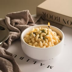 a white bowl filled with macaroni and cheese on top of a table next to a book