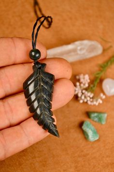 a person holding a leaf shaped pendant in their hand next to some stones and flowers