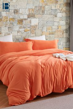 an orange comforter on a bed in front of a stone wall