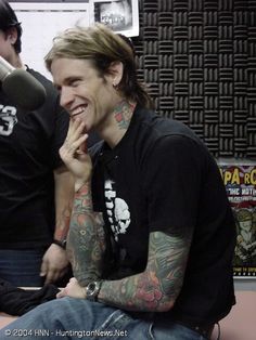 a man with long hair and tattoos sitting in front of a microphone