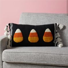 a black and orange pillow sitting on top of a gray couch next to a pink wall