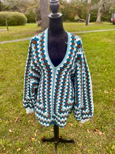 a crocheted jacket is on a mannequin in the grass near a tree