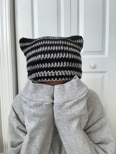 the back of a person wearing a knitted black and white striped cat hat, standing in front of a door