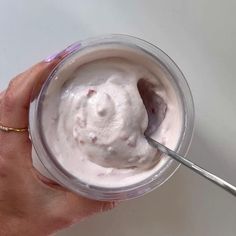 a hand holding a spoon in a cup filled with whipped cream