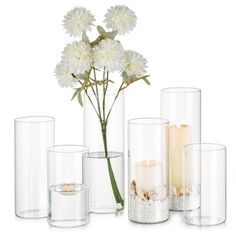 white flowers and candles in glass vases with sand on the ground next to them