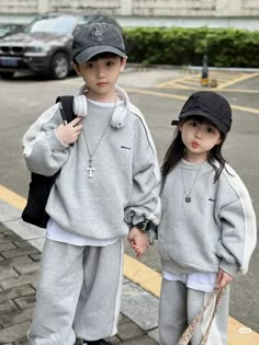 two young children standing next to each other wearing headphones and grey sweatsuits