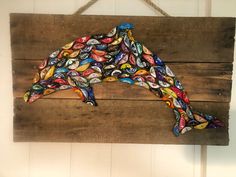 a dolphin made out of bottle caps hanging on a wooden plank with string attached to it