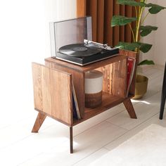 a record player sitting on top of a wooden cabinet next to a potted plant