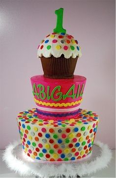 a three tiered birthday cake decorated with polka dots and a cupcake on top