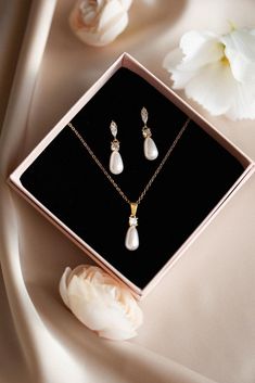 a necklace and earring set in a gift box on a table next to flowers