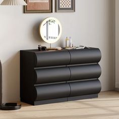 a black dresser sitting next to a wall with pictures on it and a round mirror