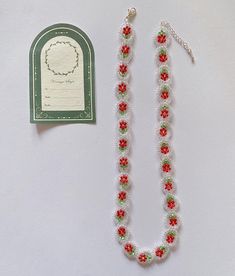 a beaded necklace with red and green flowers on it next to a small tag