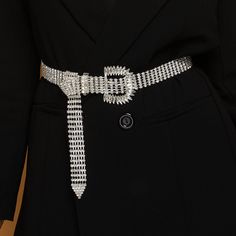 a woman wearing a black coat and silver belt with white beads on the buckles