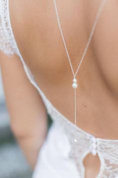 the back of a woman's white dress with a silver necklace on her neck