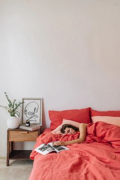 a woman laying in bed with an orange comforter and red sheets on the bed