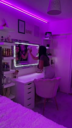 a woman sitting at a desk in front of a mirror with purple lights on it