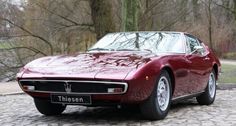 a red sports car parked on top of a cobblestone road next to trees