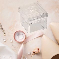 a clear box with a ring on it next to some pearls and other jewelry items