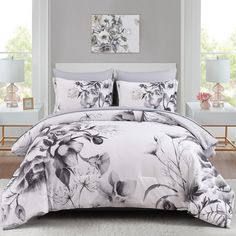 a white and black floral comforter set with two lamps on either side of the bed