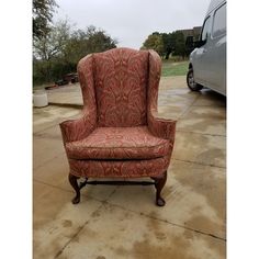 an orange and red chair sitting on top of a cement floor next to a van