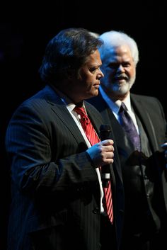 two men standing next to each other on stage with microphones in their hands and one man wearing a suit