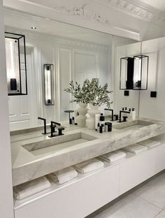 a bathroom with double sinks and mirrors in the wall, along with two vases filled with flowers