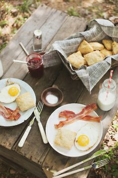 two plates with eggs, bacon and biscuits on them sitting on a picnic table outside