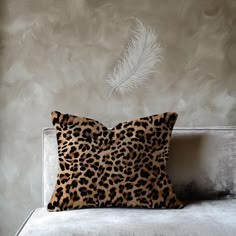 a leopard print pillow sitting on top of a couch next to a white feather wallpaper