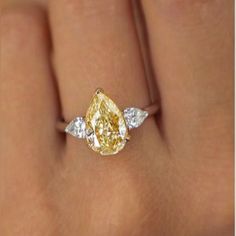 a woman's hand with a yellow and white diamond ring on top of it