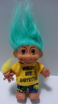 a troll doll with green hair and blue eyes holding a yellow babysitter toy