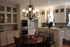 a kitchen with white cabinets and an island in front of the stove top oven is lit by two chandeliers