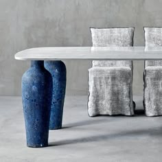 a white table with four blue vases sitting next to it on top of a cement floor