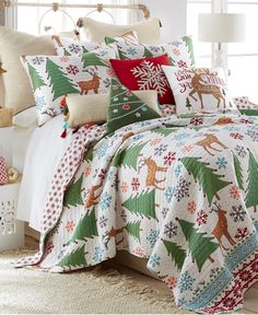 a bed covered in christmas themed comforters and pillows with deers on them, sitting next to a window