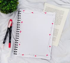 an open notebook with hearts on it next to two pens and a potted plant