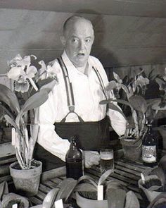 an old man standing in front of some potted plants and holding a basket with flowers on it