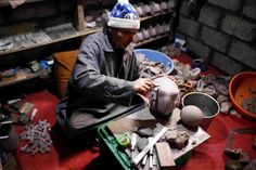 a man is working on pottery in his studio, with other items scattered around him