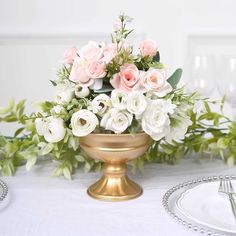 a vase filled with white and pink flowers on top of a table next to silver plates